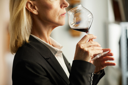 Side view closeup of female sommelier holding wine glass during tasting session, copy spaceの写真素材