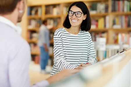 Positive woman chatting with friend in bookstore