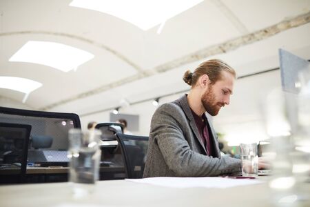 Side view portrait of handsome bearded businessman using laptop while working in open space office