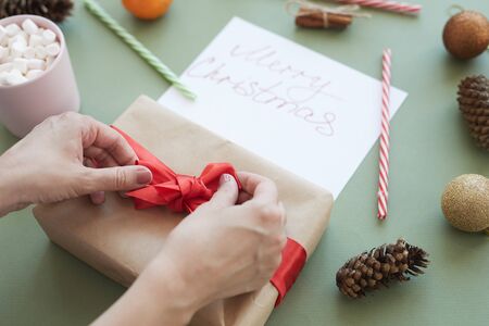 Close-up of unrecognizable woman tying bow on gift box while preparing for Christmas