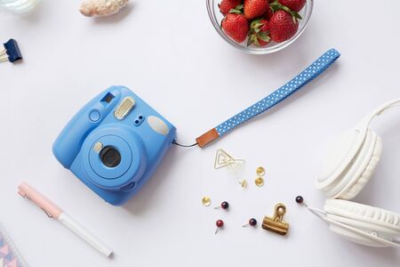 Above view of white background with instant camera, headphones, clips and pins, copy space