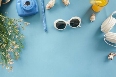 Blue background with vacation stuff such as stylish sunglasses, instant camera, grass, cocktail and shellsの写真素材