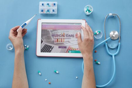 Directly above view of unrecognizable woman holding thermometer while checking health with medical websiteの写真素材