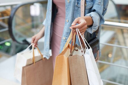 Young woman holding paper shopping bags in her hands while going shopping in new big mallの写真素材