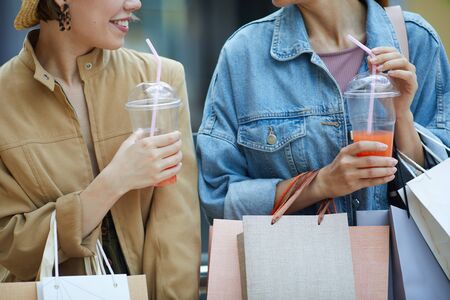 Close-up of young ladies with many paper bags drinking refreshing summer cocktails during shoppingの写真素材