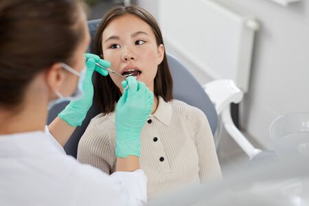 High angle portrait of Asian girl lying in dental chair with female dentist examining teeth, copy spaceの写真素材