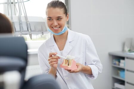 Portrait of smiling female dentist holding tooth model and consulting patient in clinic, copy spaceの写真素材