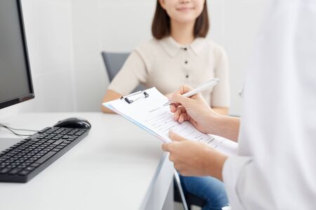 Closeup of unrecognizable doctor holding clipboard and filling patients form during consultation, copy spaceの写真素材