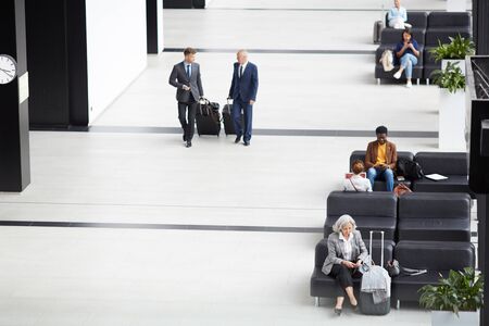 Above view of business employees in suits moving to gates of departure area, other people sitting on sofasの写真素材
