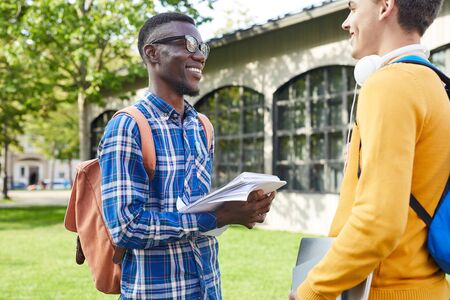 Waist up portrait of cheerful African-American student talking to friend outdoors in college campus,...