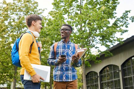 Portrait of African-American student talking to friend while walking outdoors in college campus,...