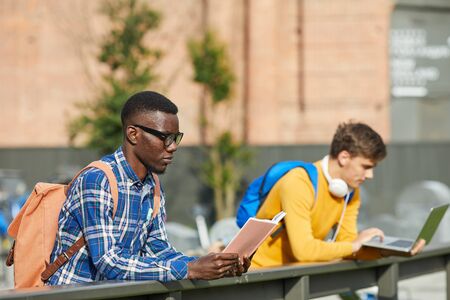 Portrait of African-American student reading book outdoors in sunlight, copy spaceの写真素材