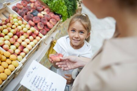 High angle portrait of cute little girl smiling at mom while shopping at farmers market together, copy spaceの写真素材