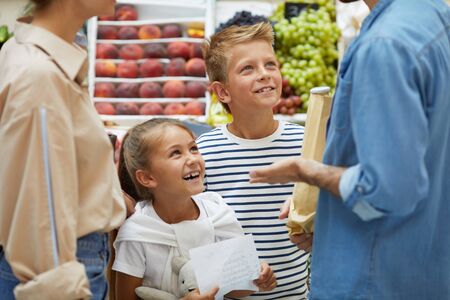 Portrait of two happy children enjoying shopping at farmers market with parents, copy spaceの写真素材