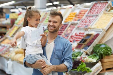 Waist up portrait of smiling father shopping with little girl at farmers market, copy spaceの写真素材