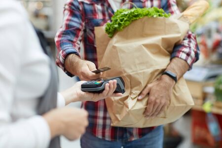 Mid section portrait of young man paying via smartphone at farmers market, copy spaceの写真素材