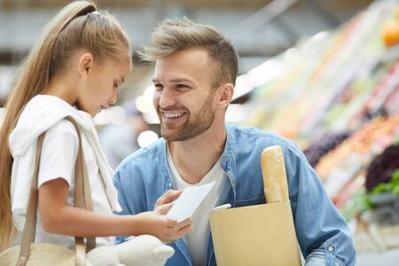 Portrait of handsome young man smiling at little girl while shopping at farmers market, copy spaceの写真素材