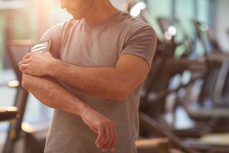 Mid-section portrait of muscular man checking smartphone in arm holder during workout in gym, copy spaceの写真素材