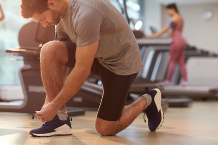 Side view portrait of muscular man tying shoelaces in gym, copy space