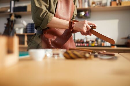 Cropped portrait of female craftsman working with leather in tannery shop lit by sunlight, copy spaceの写真素材