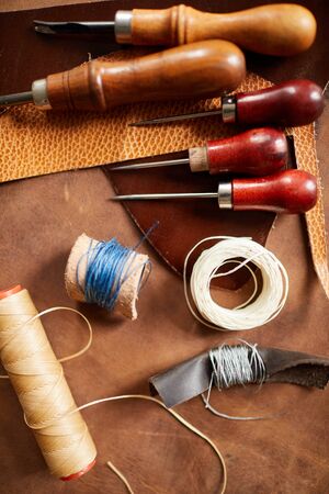 Top view background of various tools lying on real leather in leatherworking shop, copy space