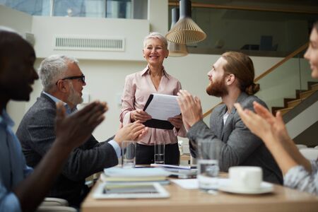 Portrait of smiling senior businessman leading meeting with employees in office and holding clipboard, copy spaceの写真素材