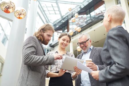 Low angle view at group of smiling business people discussing work standing in office hall, copy...