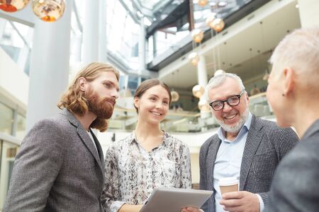 Waist up of smiling business people discussing work standing in office hall, copy spaceの写真素材