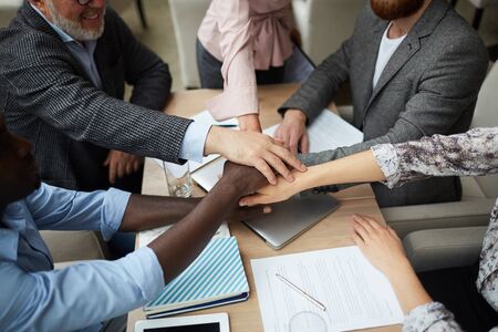 High angle closeup of diverse business team stacking hands while huddling over meeting table in...