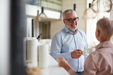 Portrait of two senior business people , man and woman, talking cheerfully at coffee break in...
