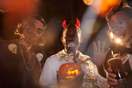 Group of adult men wearing Halloween costumes posing during party in club, focus on African-American...