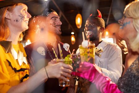 Multi-ethnic group of friends wearing Halloween costumes drinking cocktails while enjoying party in club and having funの写真素材