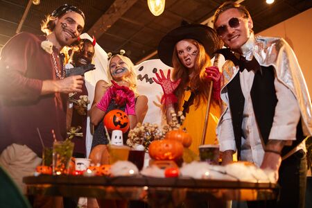 Low angle portrait of adult people wearing Halloween costumes posing making faces at camera during party in nightclub, copy spaceの写真素材