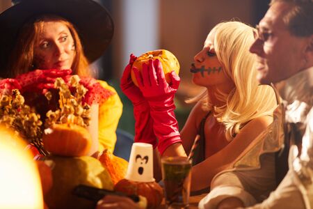 Side view portrait of young woman wearing Halloween costume kissing pumpkin during party with friends, copy spaceの写真素材