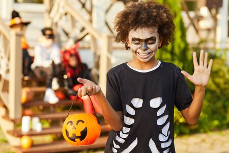 Waist up portrait of African-American boy wearing Halloween costume looking at camera while posing outdoors holding pumpkin basket in trick or treat season, copy spaceの写真素材