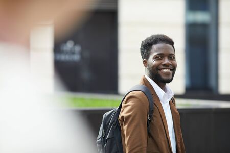 Waist up portrait of young African-American man smiling happily at camera while standing outdoors ion city street, copy spaceの写真素材