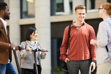 Group of contemporary young people chatting in city street, focus on handsome young man talking to friends outdoors, copy spaceの写真素材