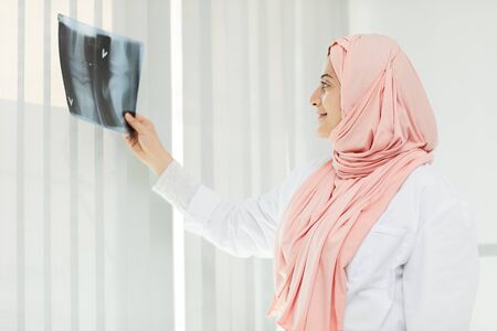 Side view portrait of Arab woman working as doctor holding X-ray image of leg joints against window, copy spaceの写真素材
