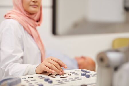 Closeup of young Arab female doctor performing ultrasound exam in medical clinic, copy spaceの写真素材