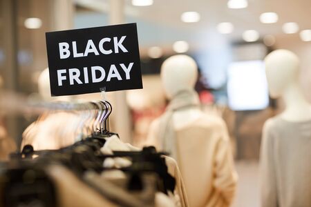 Background image of Black Friday sign on clothes rack with autumn clothes in shopping mall during...