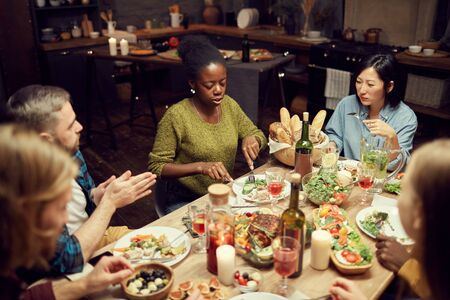 High angle view at multi-ethnic group of people sitting at dinner table together and enjoying delicious food, copy spaceの写真素材
