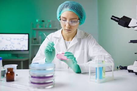 Portrait of young woman holding petri dish while working on medical research in laboratory, copy...