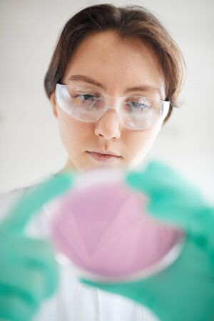 Low angle portrait of young woman holding petri dish while working on research in medical laboratoryの写真素材