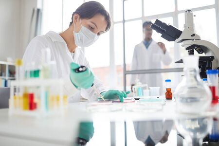 Side view portrait of young woman working in laboratory preparing test samples for medical research,...