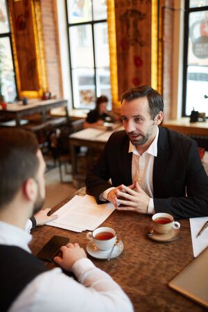 High angle view of two successful businessmen discussing deal while sitting at table in luxurious cafe, copy spaceの写真素材