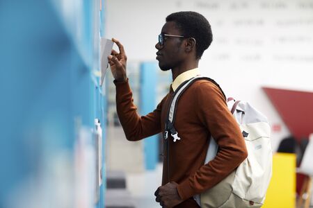 Side view portrait of African-American student choosing books standing by shelves in college...