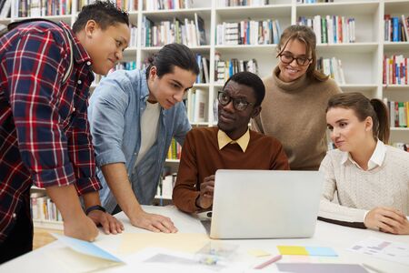 Multi-ethnic group of students studying together in college library, focus on African-American man using laptop, copy spaceの写真素材