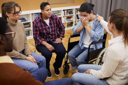 Portrait of disabled Latin-American man crying sitting in wheelchair during support group meeting,...
