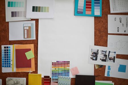 Above view of creative designers workplace: color swatches, type notes and photographs arranged on wooden table around blank paper, copy spaceの写真素材