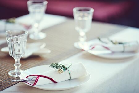 Close up of elegant table setting for Christmas dinner: white napkins tied with fir tree decor in...